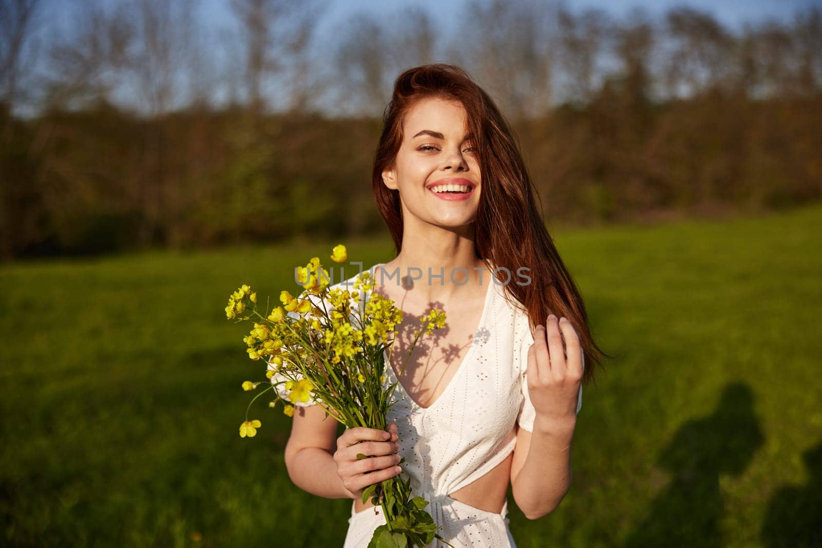 Beautiful woman in a white dress with a bouquet of yellow wildflowers walking in a field . High quality photo
