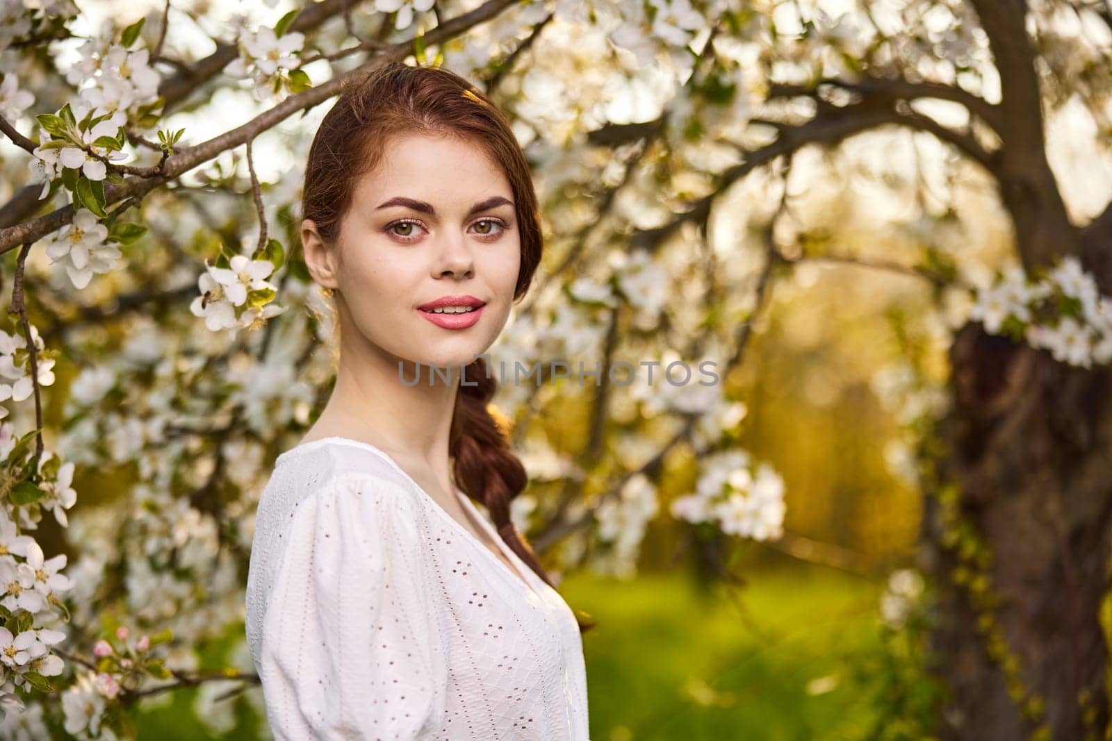 a sweet, young woman stands in a blooming garden in a light dress by Vichizh