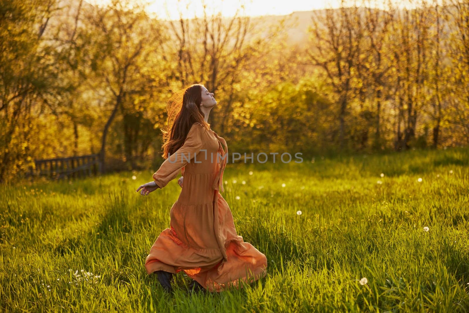 a joyful woman runs through a green field during the sunset enjoying a warm summer day and nature. Horizontal photography in nature by Vichizh