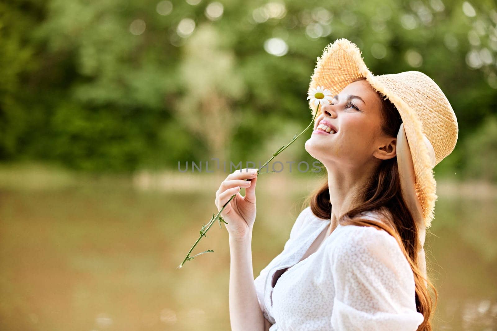 close-up portrait of a happy woman in a wicker hat with a camomile in her hands on the background of the lake by Vichizh