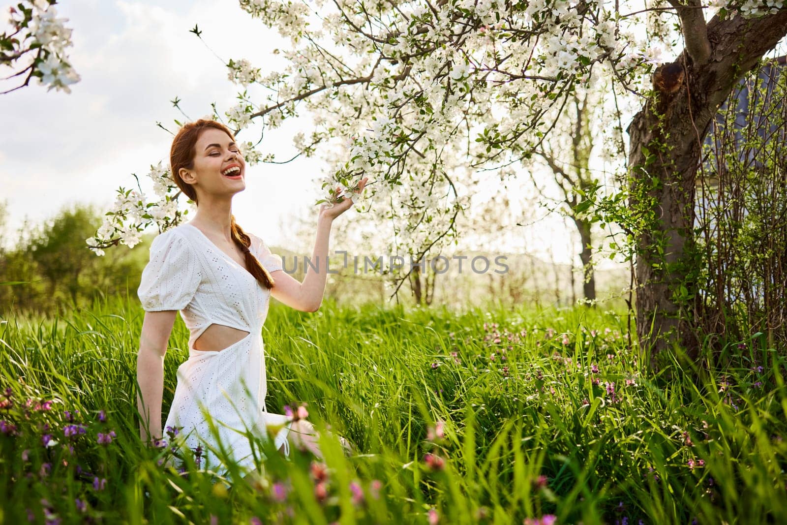 a woman in a light dress sits in the grass near a flowering apple tree by Vichizh