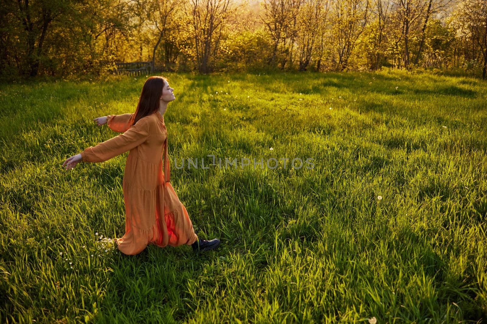 a joyful woman runs through a green field with her hands behind her back, enjoying a warm summer day and nature during the sunset. Horizontal photography in nature by Vichizh