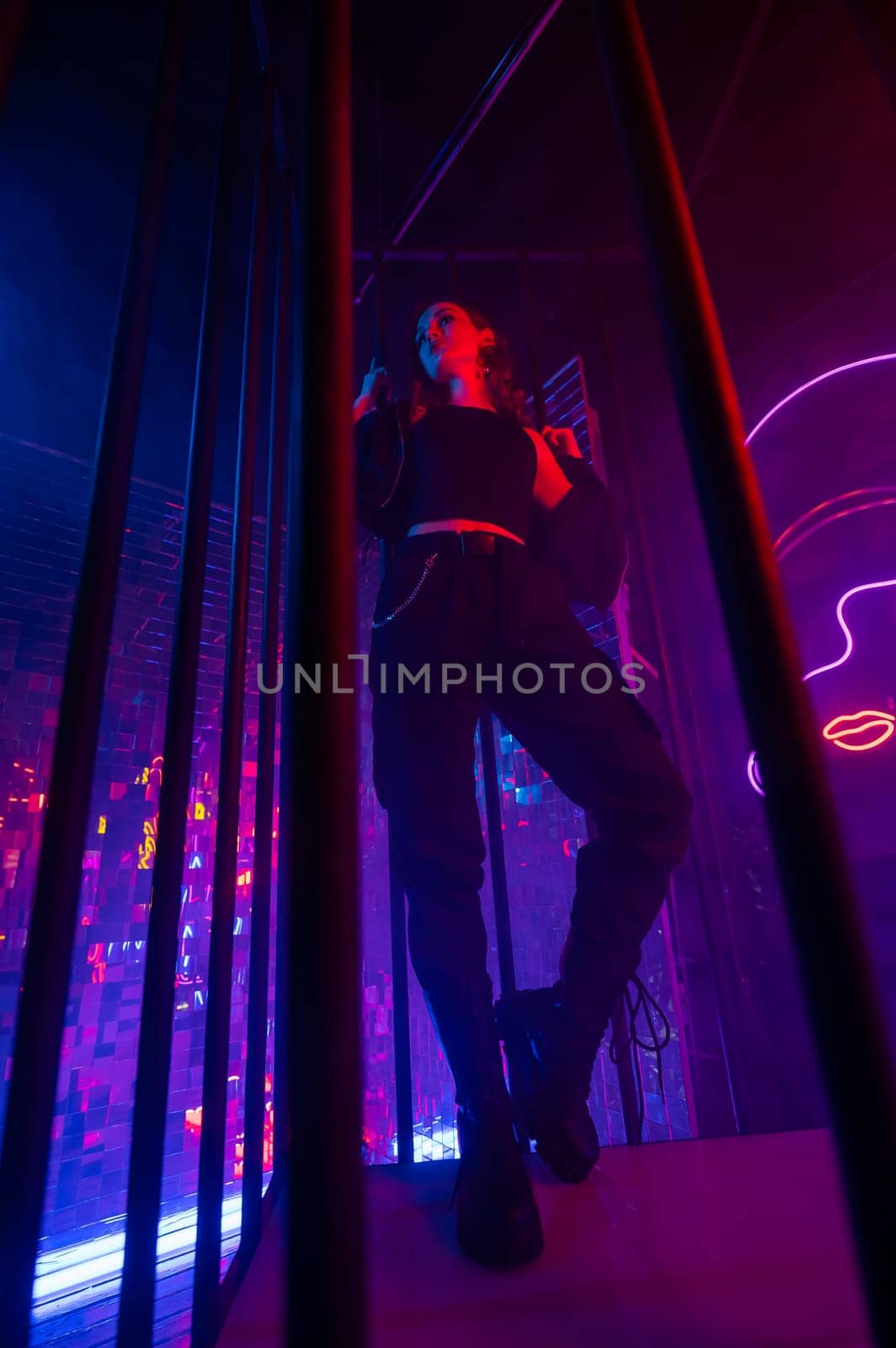 Caucasian woman in neon studio behind steel bars