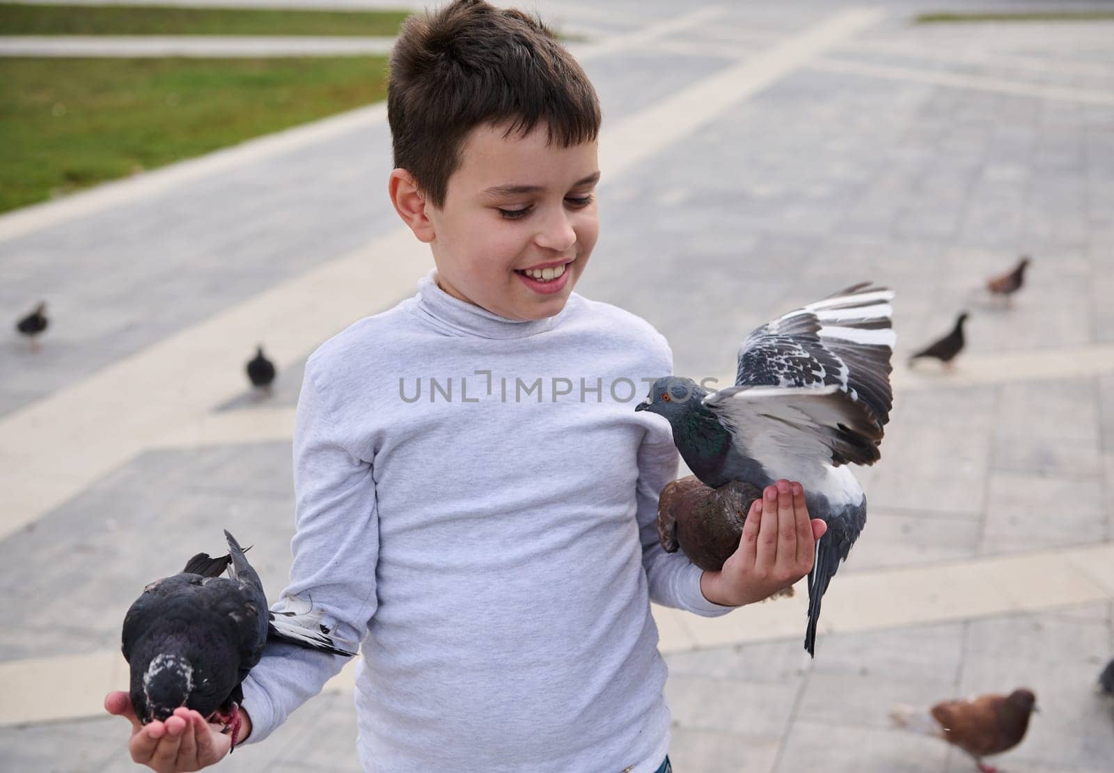 Caucasian happy child boy feeding feral pigeons in the square of a city park. Children, nature and animals concept by artgf