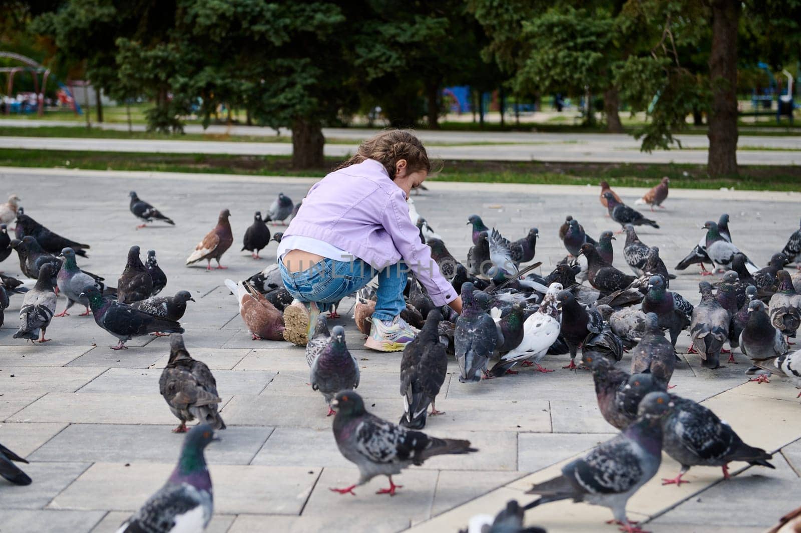 Little child girl 5 years old, feeding rock pigeons in the park square. The concept of installing of love, care and compassion for wild animals leaving in the street from childhood. People and nature