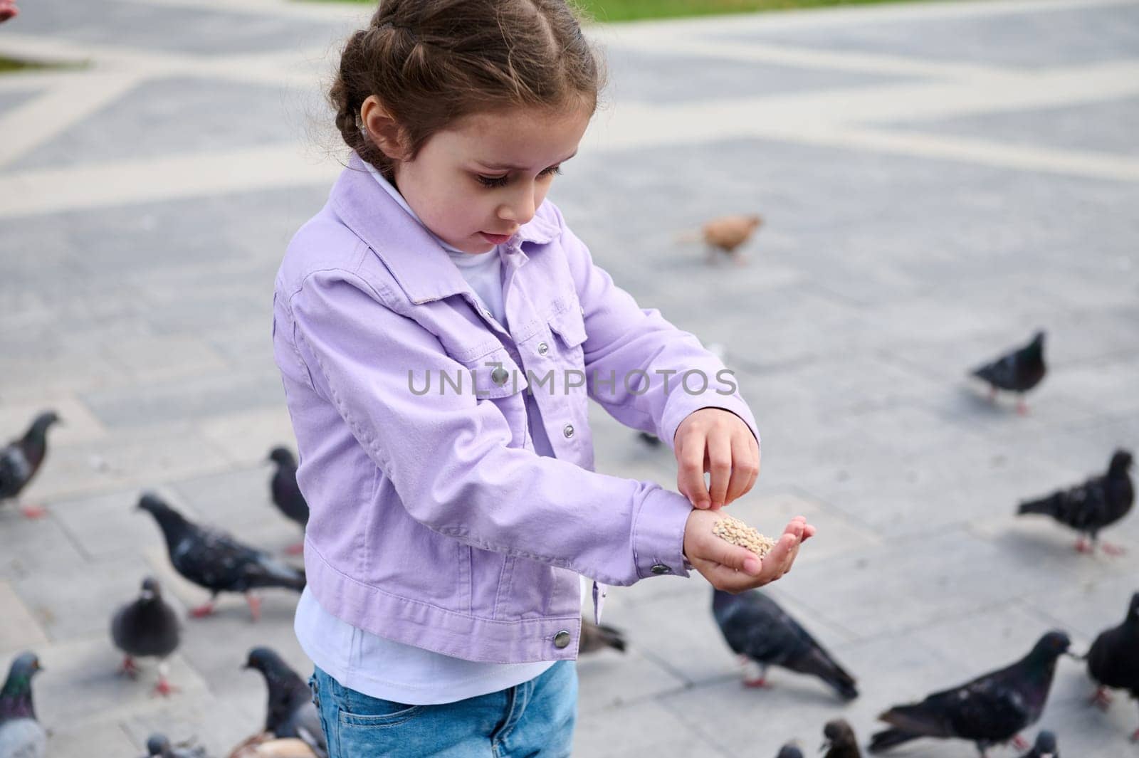 Adorable little child girl feeding rock doves in the city square. The concept of childhood, care and love for animals by artgf