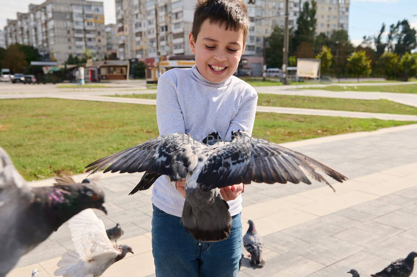Adorable child boy having fun during family outing, feeding flock of flying doves to his hands, taking care for animals by artgf