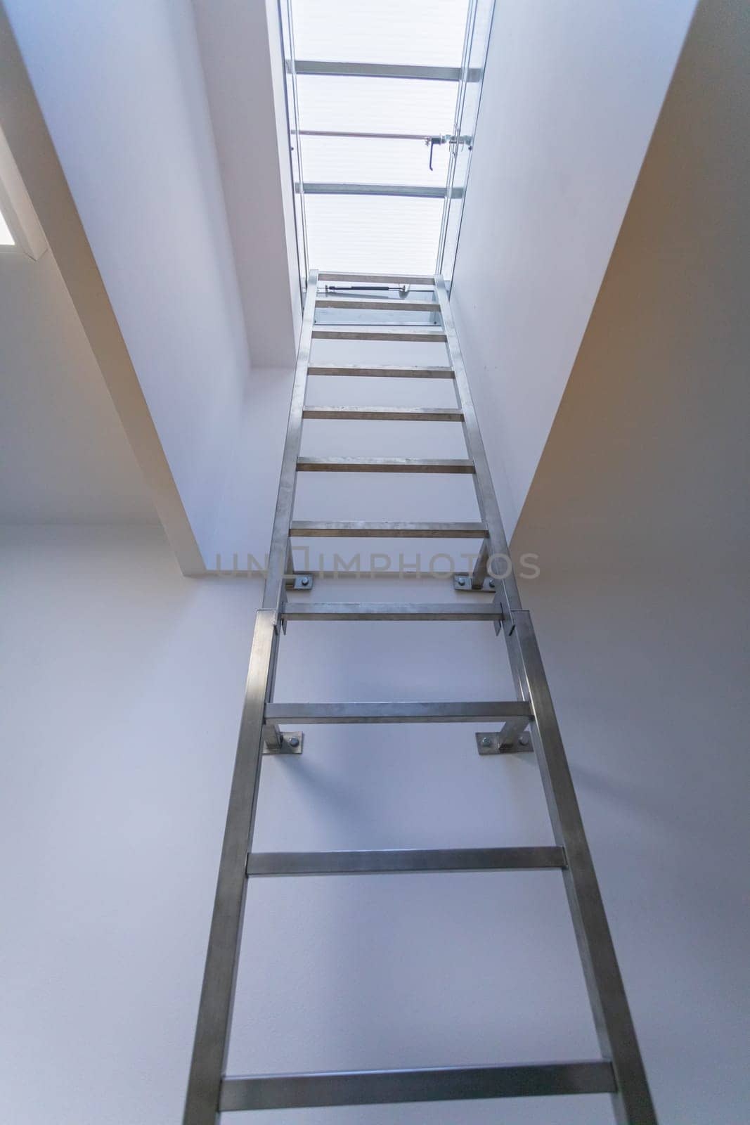 High ladder made of stainless steel and attached to the wall. Technical exit to the roof slope directly from the corridor of the building.