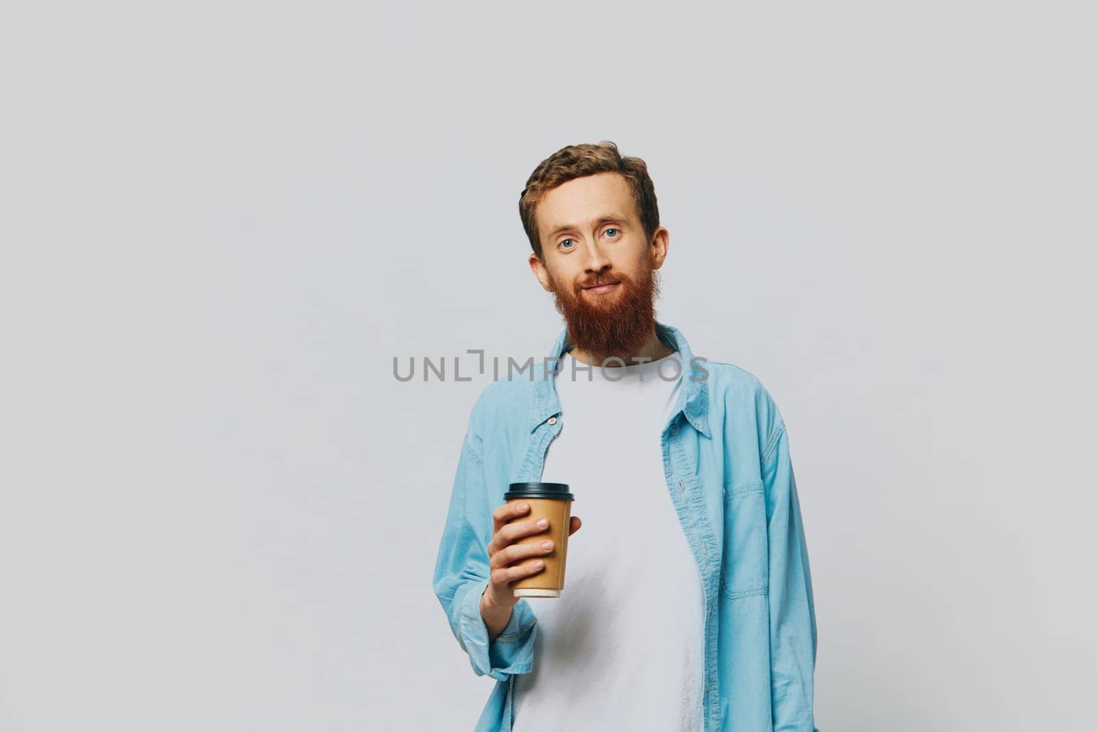 Man hipster with a cup of coffee with a smile on a gray background in a blue shirt and white t-shirt. High quality photo