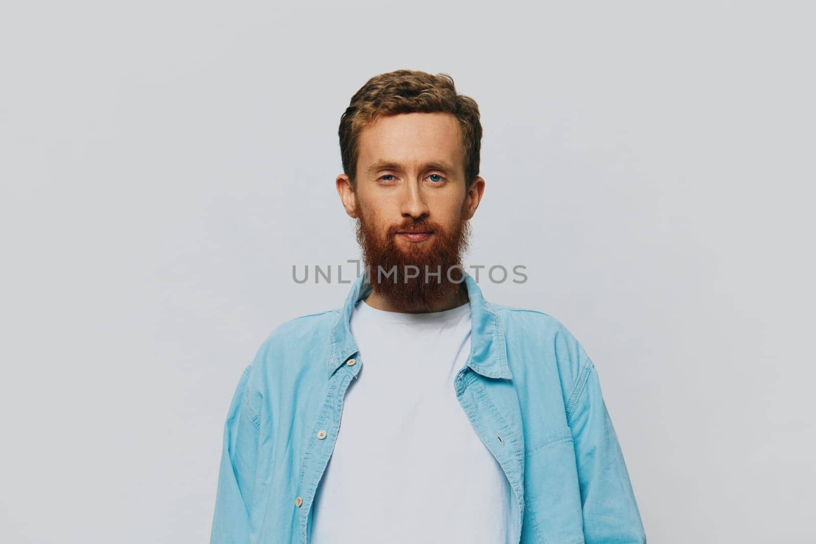 Male hipster portrait smile on gray background in blue shirt and white t-shirt, portrait of a man with a beard by SHOTPRIME