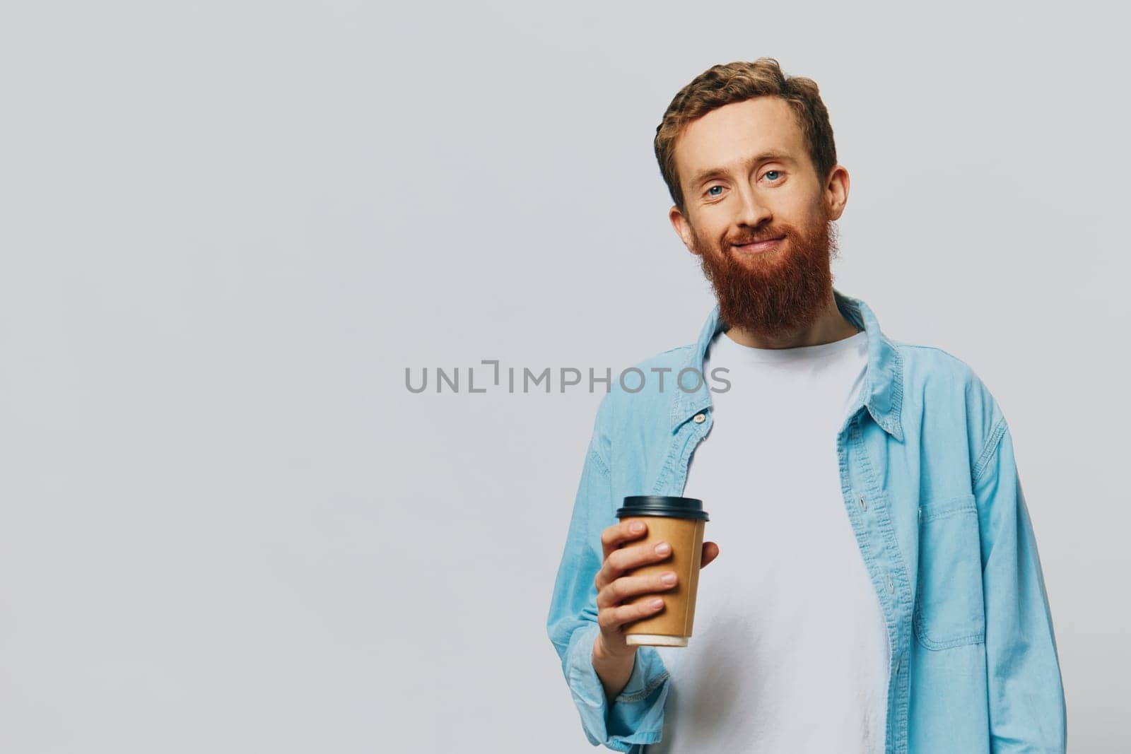 Man hipster with a cup of coffee with a smile on a gray background in a blue shirt and white t-shirt. High quality photo