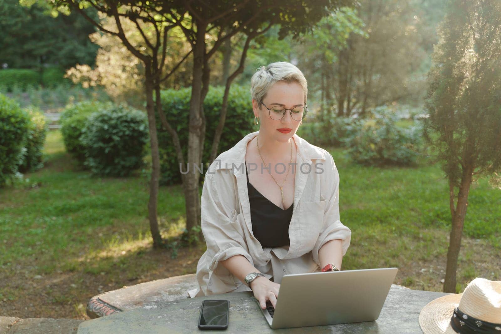 woman freelancer in glasses works at a computer at a white table in nature and spends her day productively.