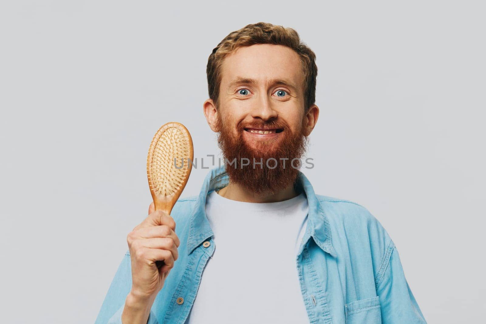 Portrait of a man with a massage comb in his hands, combing his hair and beard, hair loss problem. High quality photo