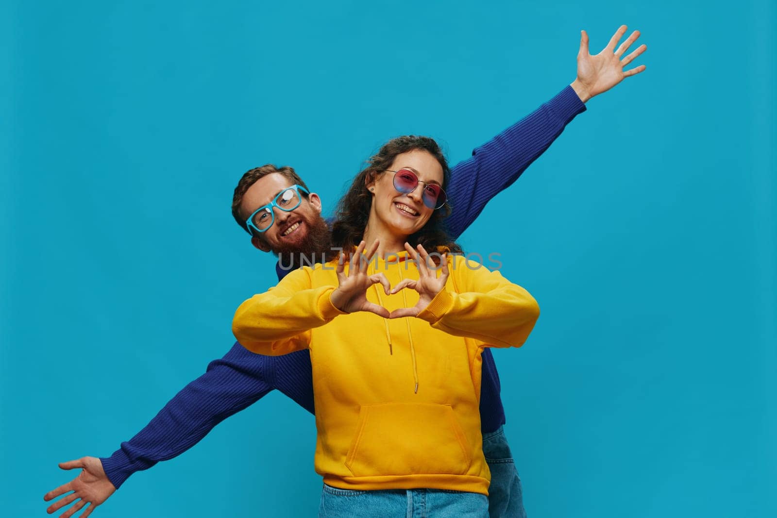 A woman and a man fun couple cranking and showing signs with their hands smiling cheerfully, on a blue background, The concept of a real relationship in a family. by SHOTPRIME