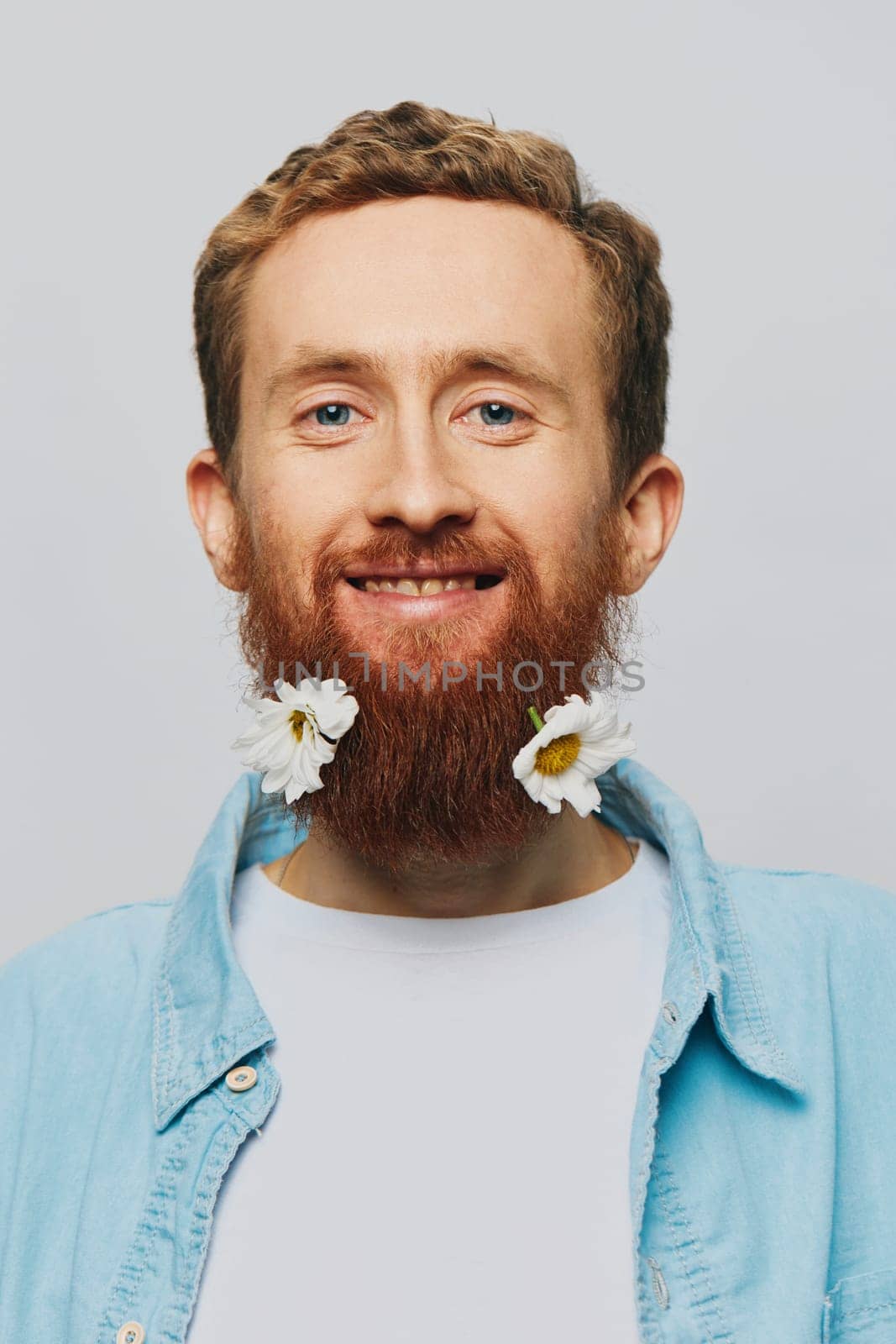 Portrait of a funny man in a white T-shirt with flowers daisies in his beard on a white isolated background, copy place. Holiday concept and congratulations. High quality photo