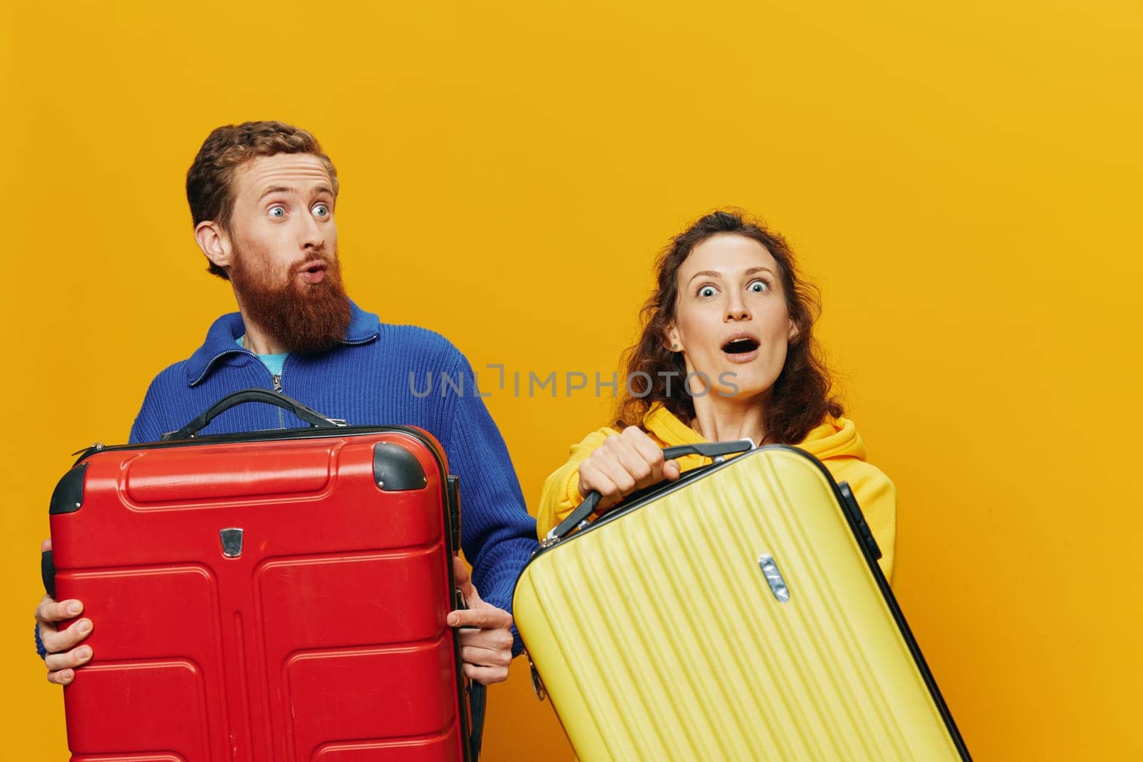 Woman and man smiling, suitcases in hand with yellow and red suitcase smiling merrily and crooked, yellow background, going on a trip, family vacation trip, newlyweds. High quality photo