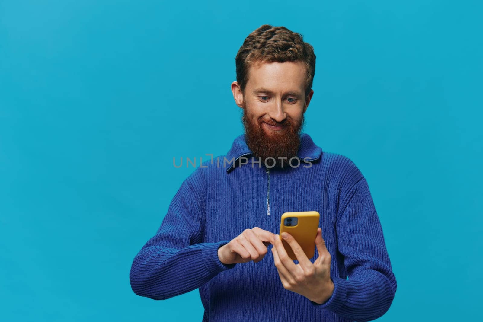 Portrait of a man with a phone in his hands does looking at it and talking on the phone, on a blue background. Communicating online social media, lifestyle. High quality photo