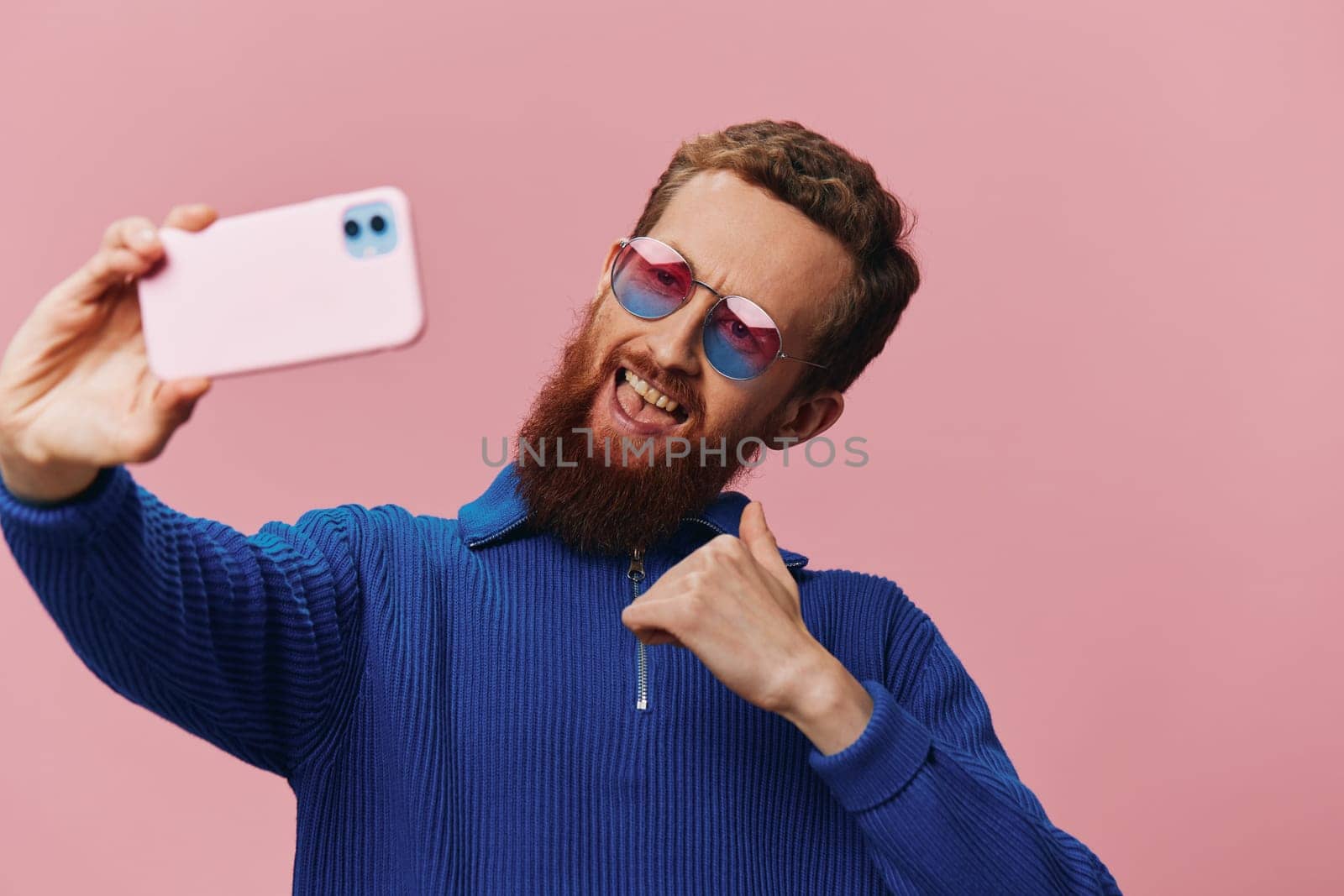 Portrait of a redheaded man with phone in hand taking selfies and photos on his phone with a smile on a pink background, blogger by SHOTPRIME