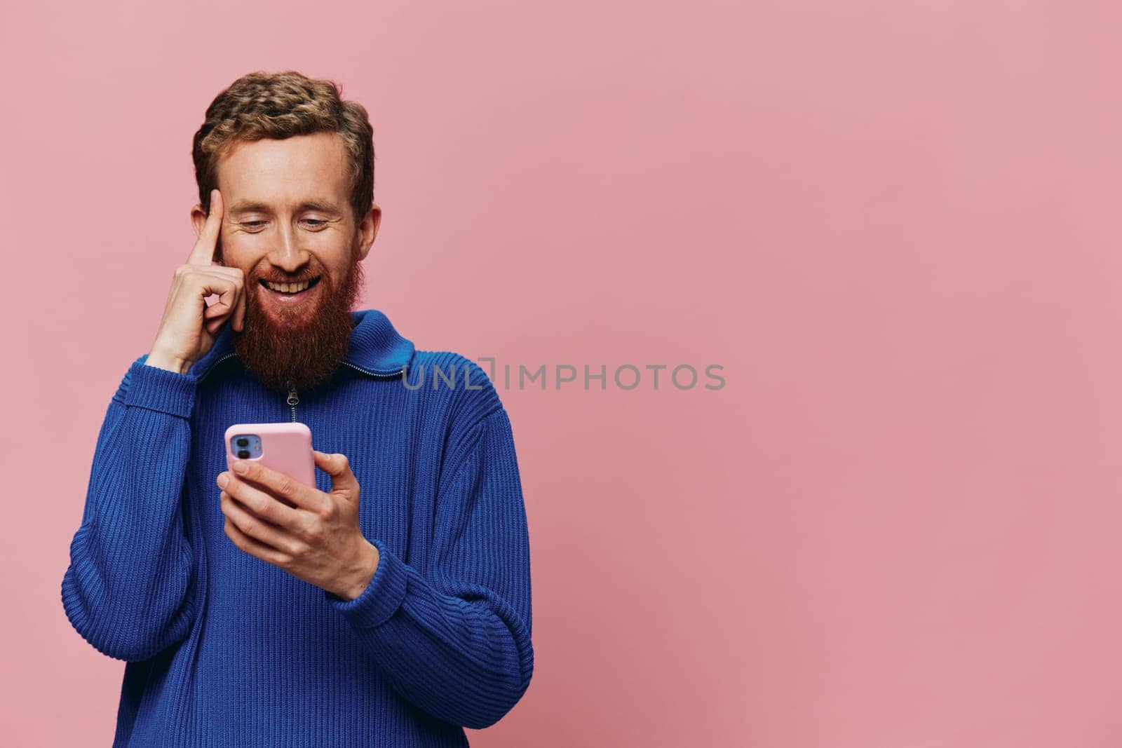 Portrait of a man with a phone in his hands doing looking at it and talking on the phone, on a pink background. Communicating online social media, lifestyle. High quality photo