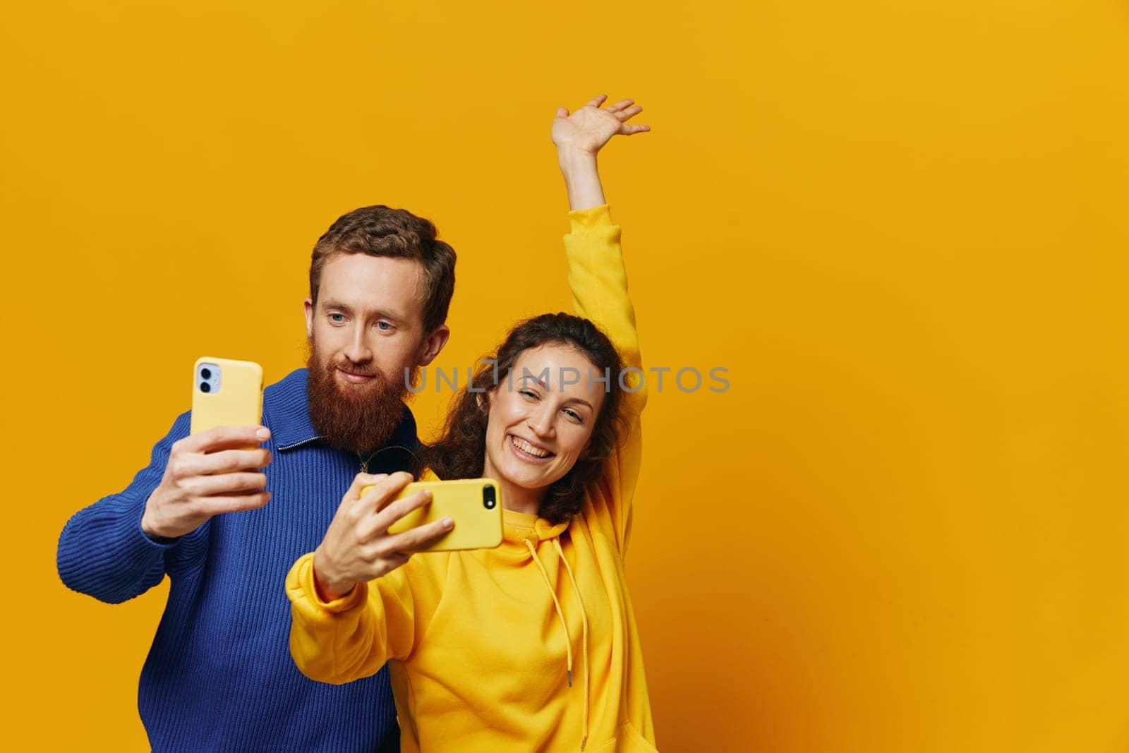 Man and woman couple smiling merrily with phone in hand social media viewing photos and videos, on yellow background, symbols signs and hand gestures, family freelancers. High quality photo