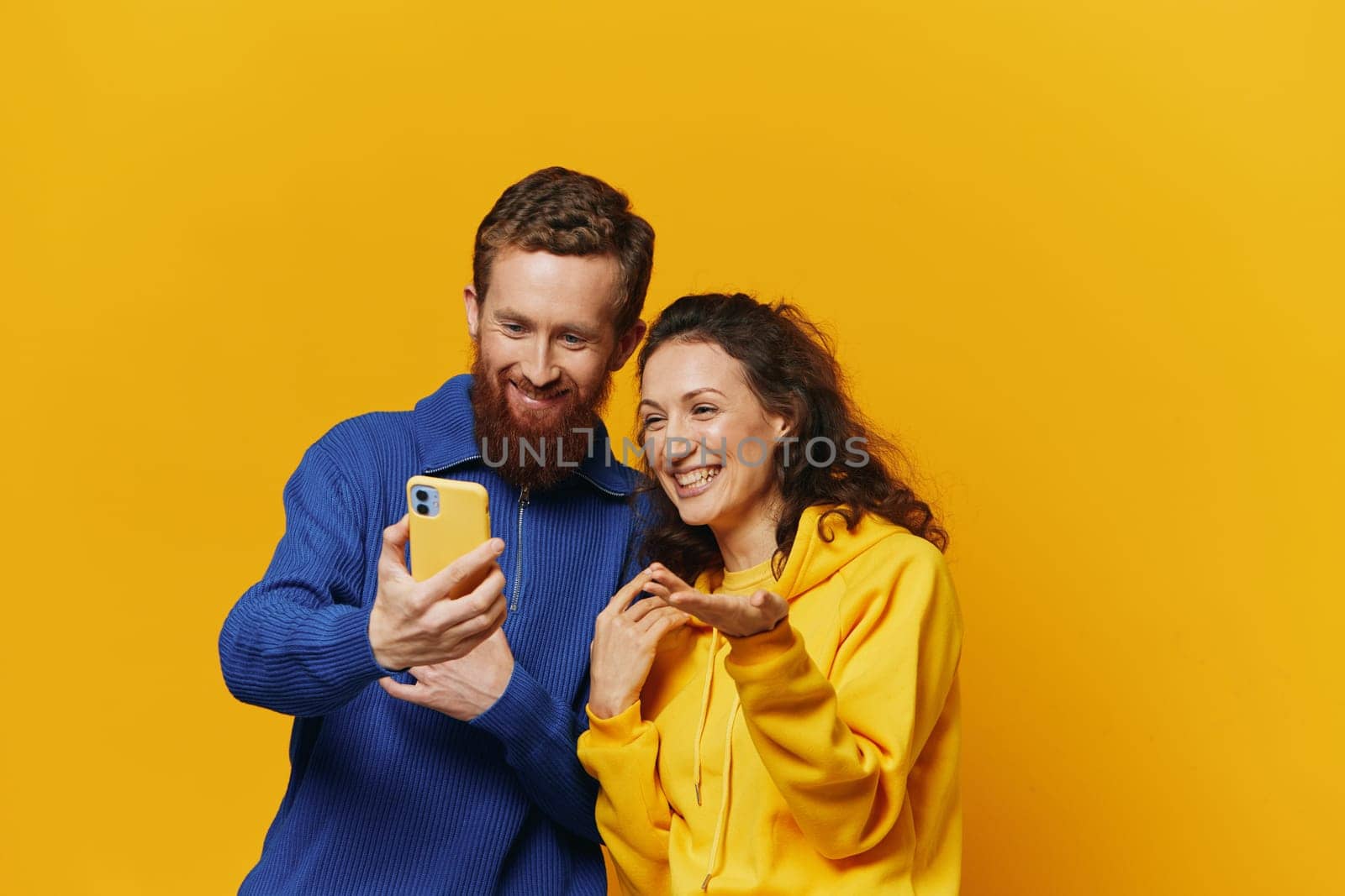 Man and woman couple smiling merrily with phone in hand social media viewing photos and videos, on yellow background, symbols signs and hand gestures, family freelancers. High quality photo