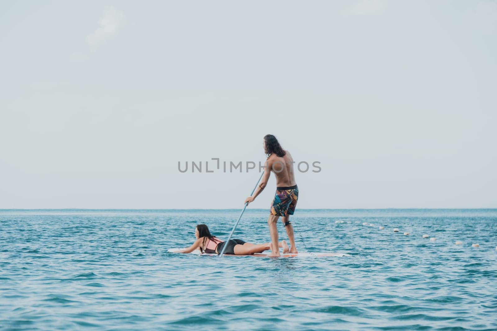 Silhouette of woman standing, surfing on SUP board, confident paddling through water surface. Idyllic sunset or sunrise. Sports active lifestyle at sea or river.