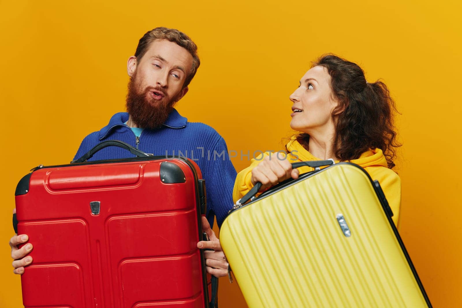 Woman and man smiling, suitcases in hand with yellow and red suitcase smiling merrily and crooked, yellow background, going on a trip, family vacation trip, newlyweds. by SHOTPRIME