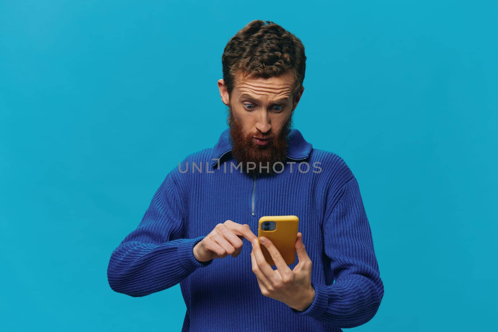 Portrait of a man with a phone in his hands does looking at it and talking on the phone, on a blue background. Communicating online social media, lifestyle. High quality photo