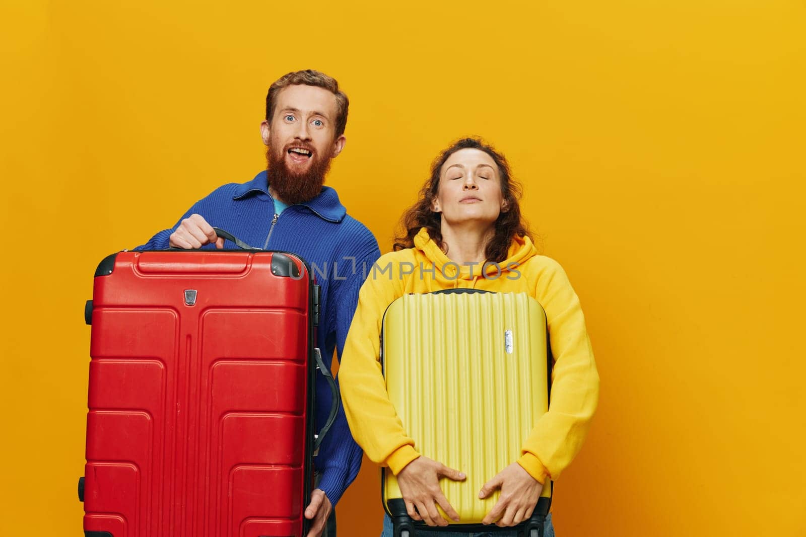 Woman and man smiling, suitcases in hand with yellow and red suitcase smiling merrily and crooked, yellow background, going on a trip, family vacation trip, newlyweds. High quality photo