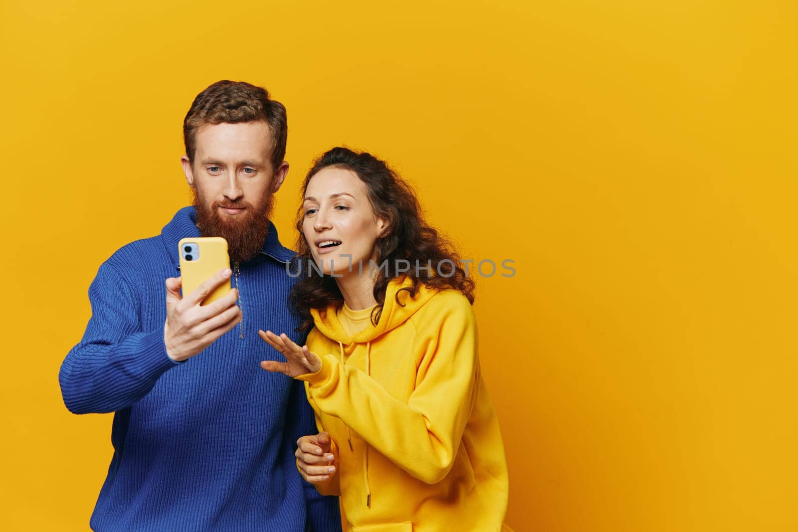 Man and woman couple smiling merrily with phone in hand social media viewing photos and videos, on yellow background, symbols signs and hand gestures, family freelancers. High quality photo