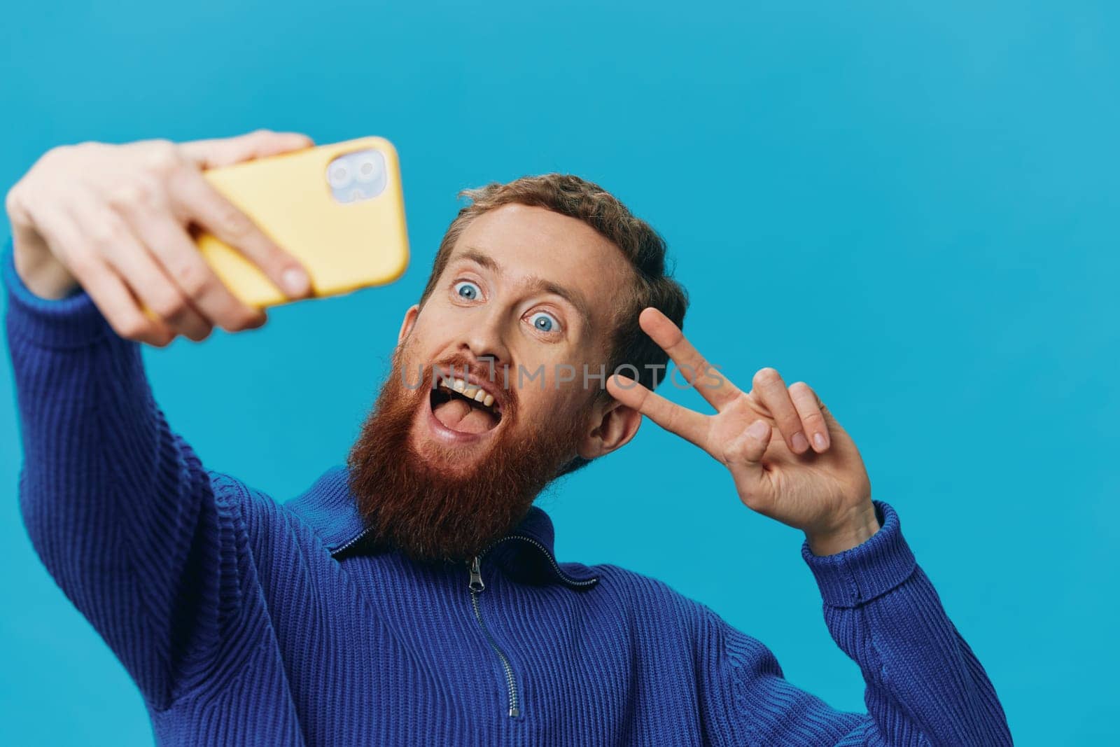 Portrait of a man with a phone in his hands blogger takes selfies, on a blue background. Communicating online social media, lifestyle by SHOTPRIME