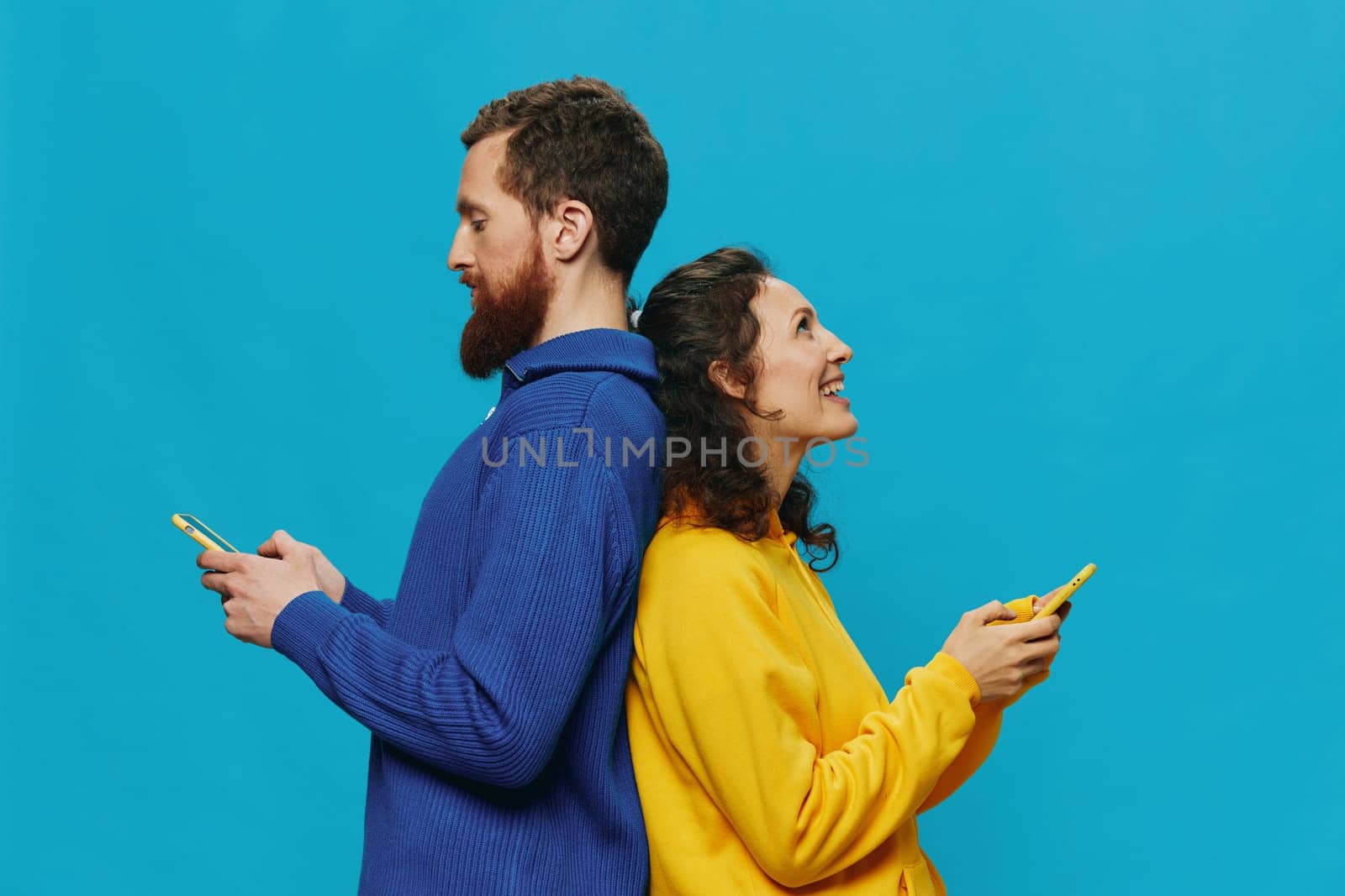 Woman and man cheerful couple with phones in their hands crooked smile cheerful, on blue background. The concept of real family relationships, talking on the phone, work online. by SHOTPRIME