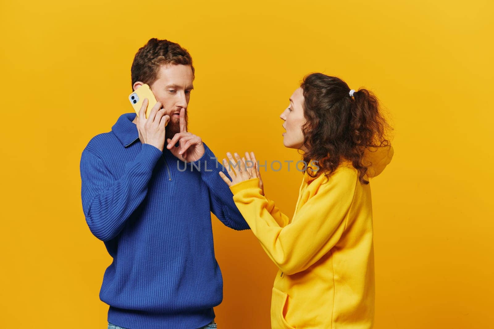 Man and woman couple with phone in hand call talking on the phone, on a yellow background, symbols signs and hand gestures, family quarrel jealousy and scandal. High quality photo