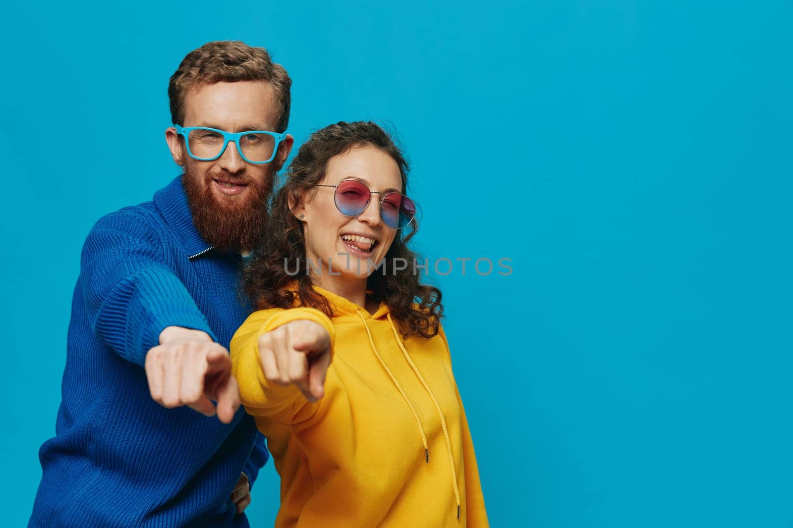 A woman and a man fun couple cranking and showing signs with their hands smiling cheerfully, on a blue background, The concept of a real relationship in a family. by SHOTPRIME