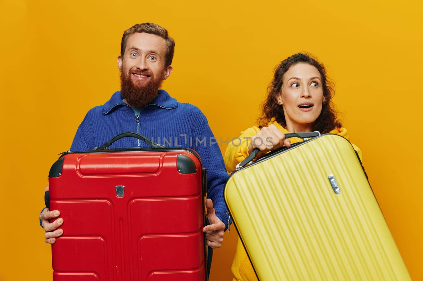 Woman and man smiling, suitcases in hand with yellow and red suitcase smiling merrily and crooked, yellow background, going on a trip, family vacation trip, newlyweds. High quality photo