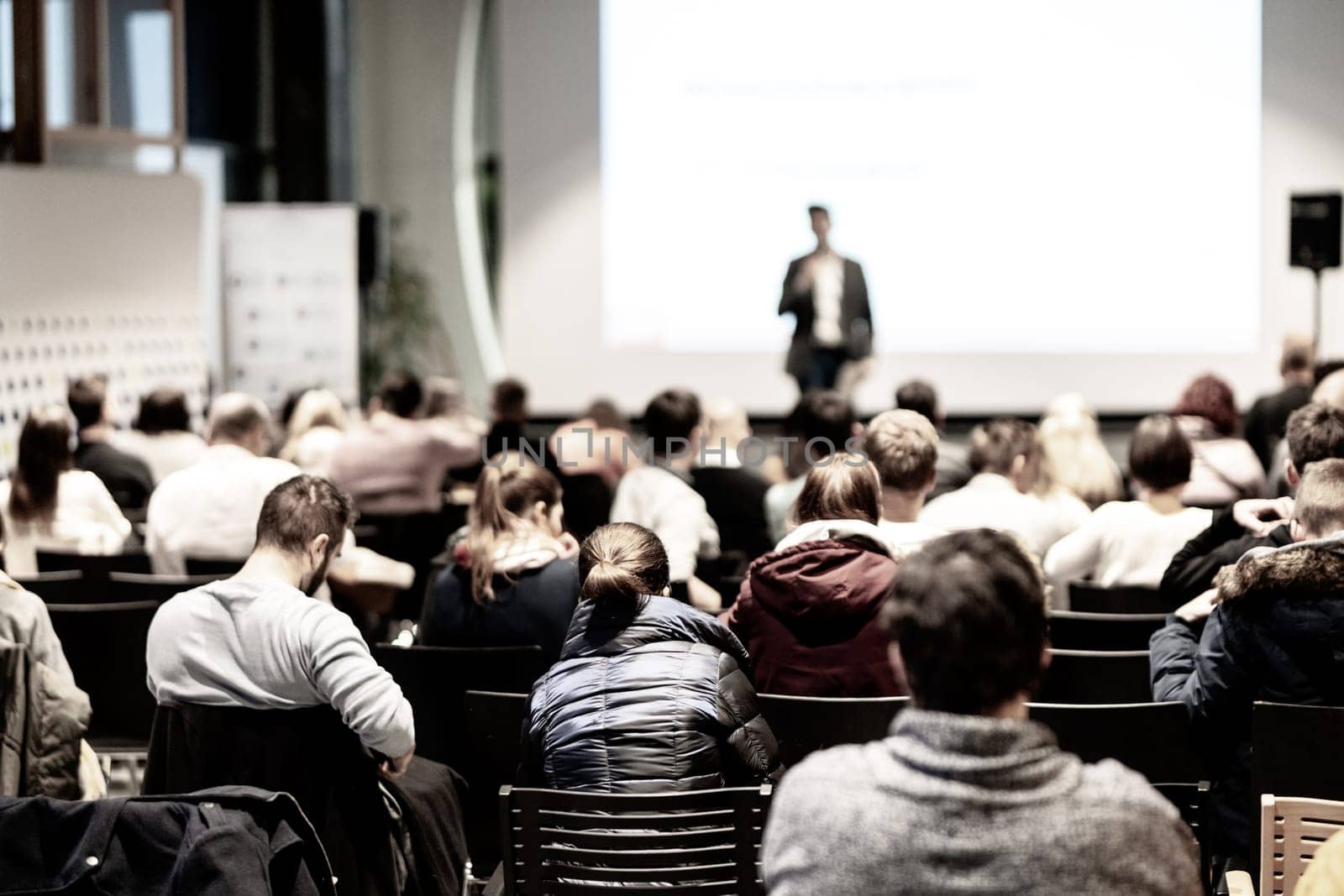 Speaker giving a talk in conference hall at business event. Audience at the conference hall. Business and Entrepreneurship concept. Focus on unrecognizable people in audience.