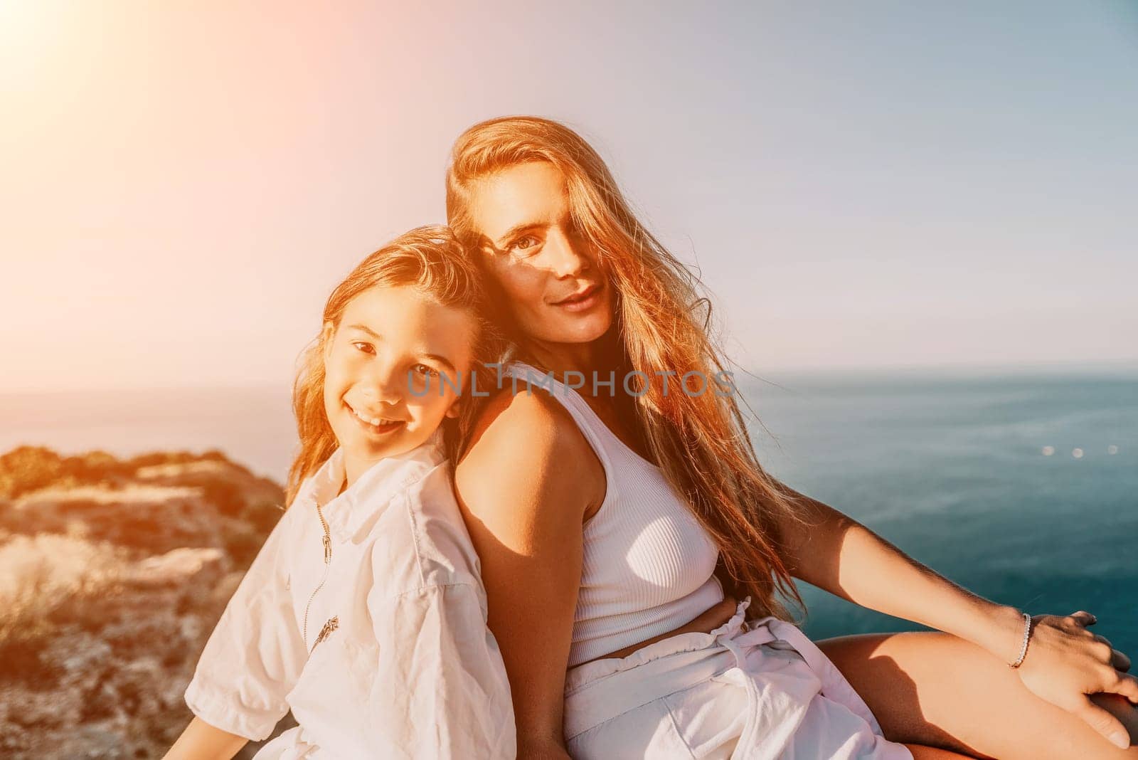 Close up portrait of mom and her teenage daughter hugging and smiling together over sunset sea view. Beautiful woman relaxing with her child.