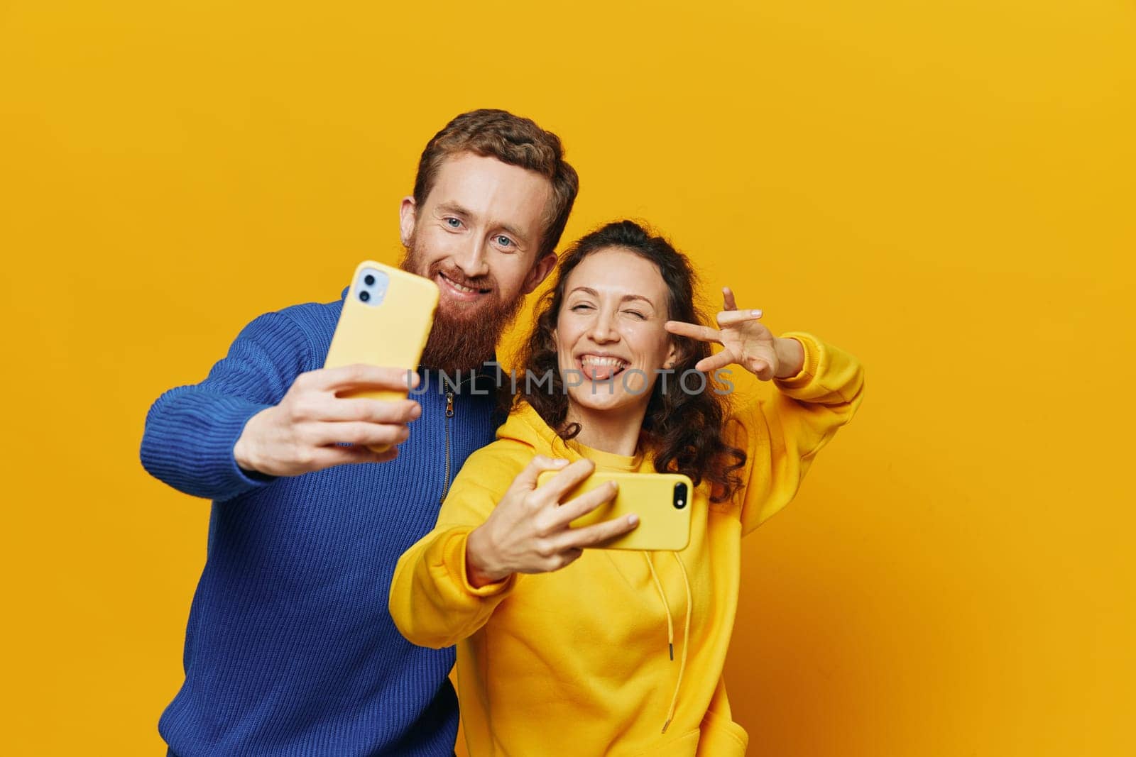 Man and woman couple smiling merrily with phone in hand social media viewing photos and videos, on yellow background, symbols signs and hand gestures, family freelancers. High quality photo