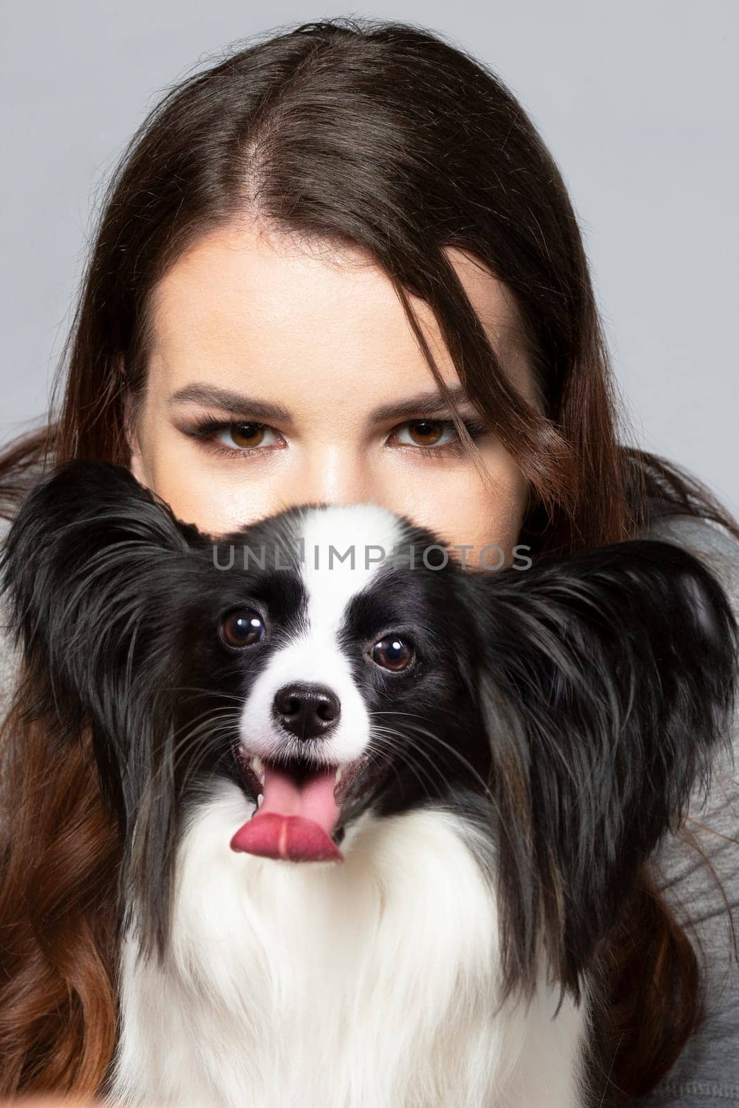 A cute young woman is hugging her papillon puppy. The eyes of a beautiful girl and the eyes of a funny dog with big ears.