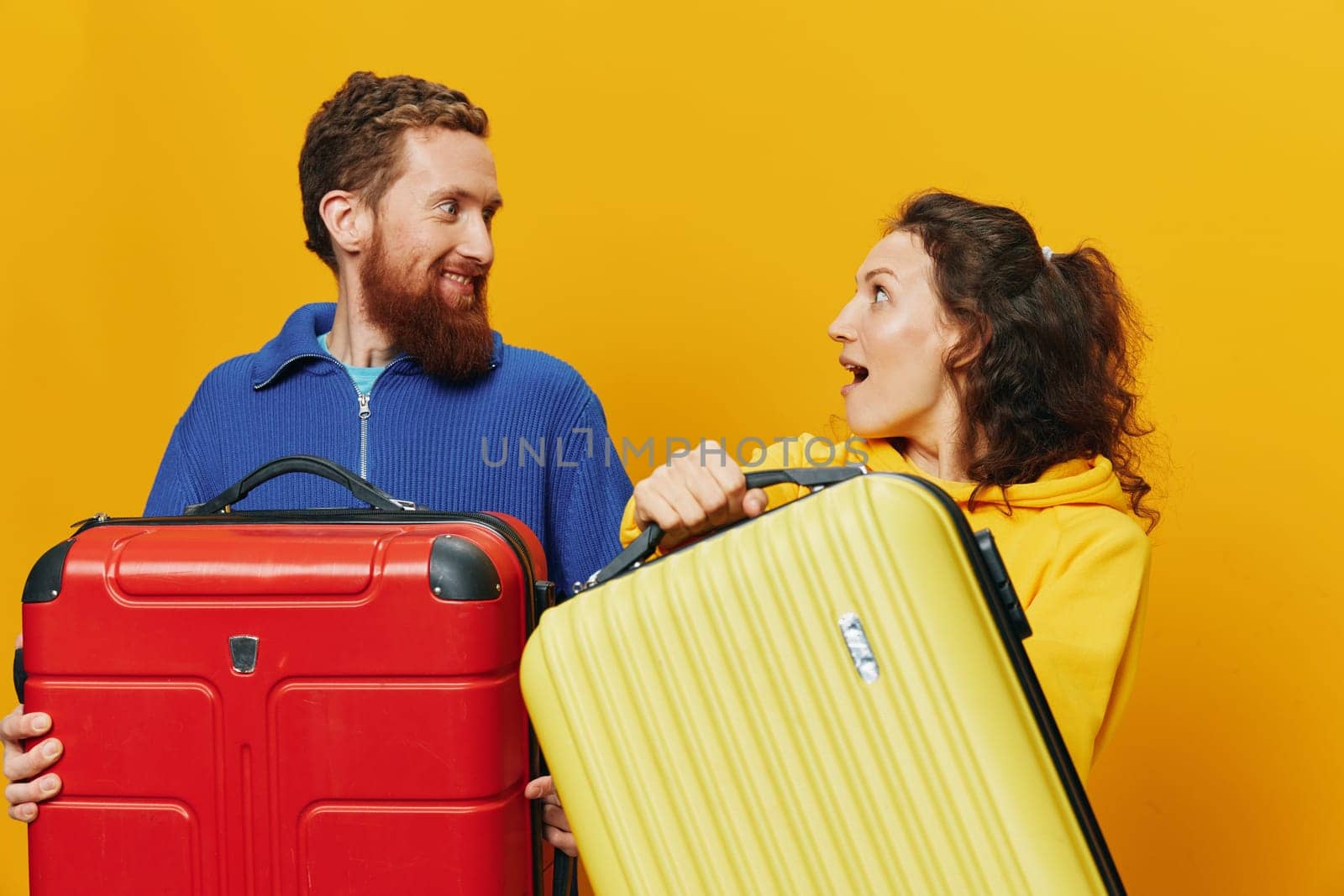 Woman and man smiling, suitcases in hand with yellow and red suitcase smiling merrily and crooked, yellow background, going on a trip, family vacation trip, newlyweds. High quality photo