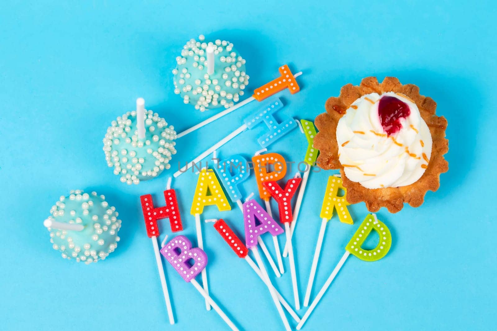 Cakes and cupcakes with rainbow-colored birthday candles with the words Happy Birthday. Anniversary celebration.