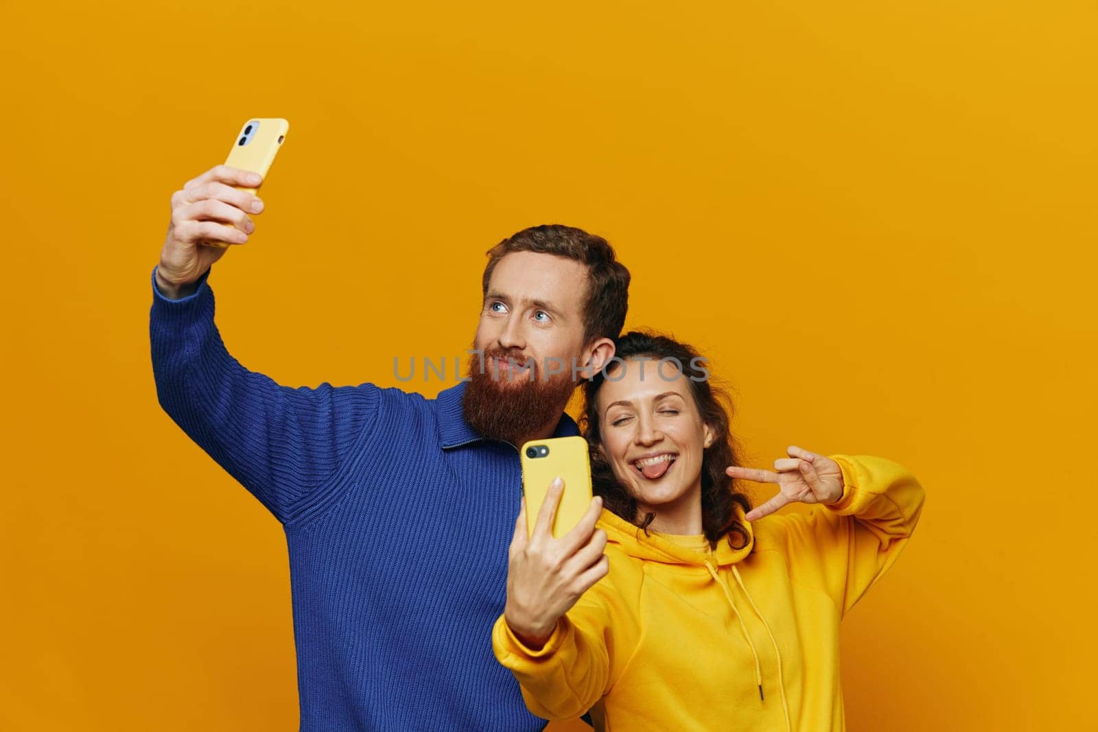 Man and woman couple smiling merrily with phone in hand social media viewing photos and videos, on yellow background, symbols signs and hand gestures, family freelancers. by SHOTPRIME