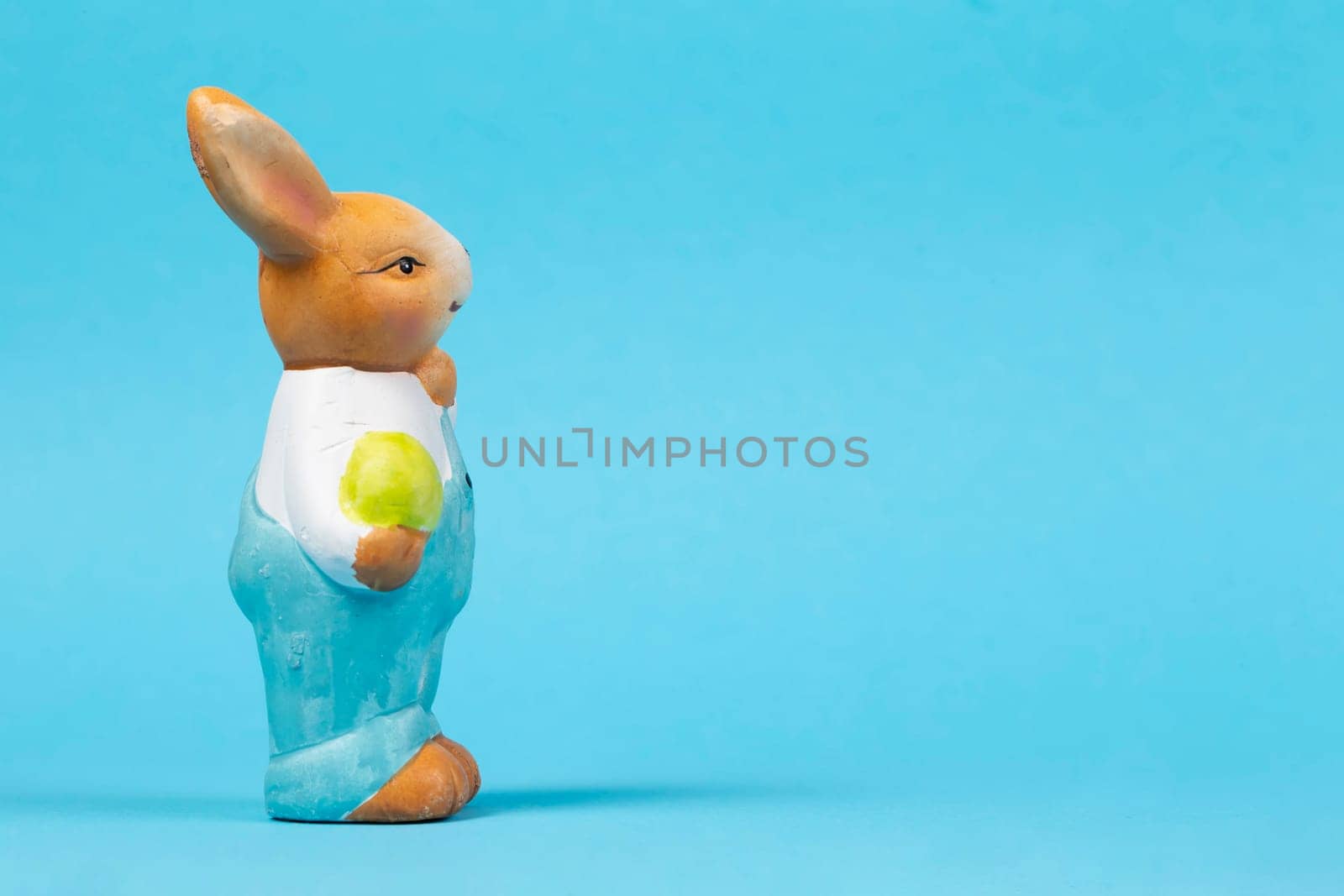 Figure of a teddy Easter bunny with an egg on a blue background. Easter card.