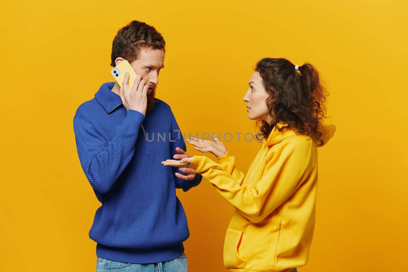 Man and woman couple with phone in hand call talking on the phone, on a yellow background, symbols signs and hand gestures, family quarrel jealousy and scandal. High quality photo