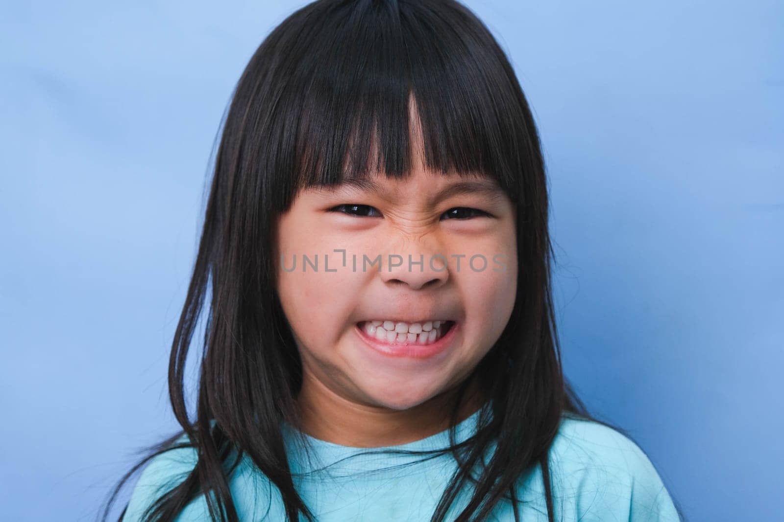 Close-up of smiling young girl revealing her beautiful white teeth on a blue background. Concept of good health in childhood.