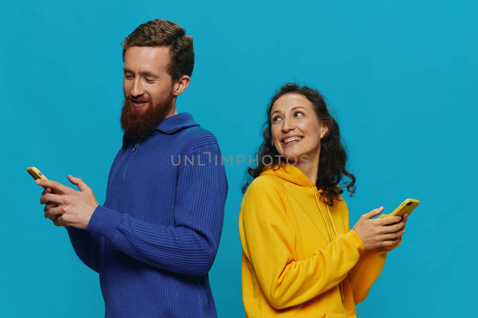 Woman and man cheerful couple with phones in their hands crooked smile cheerful, on blue background. The concept of real family relationships, talking on the phone, work online. High quality photo