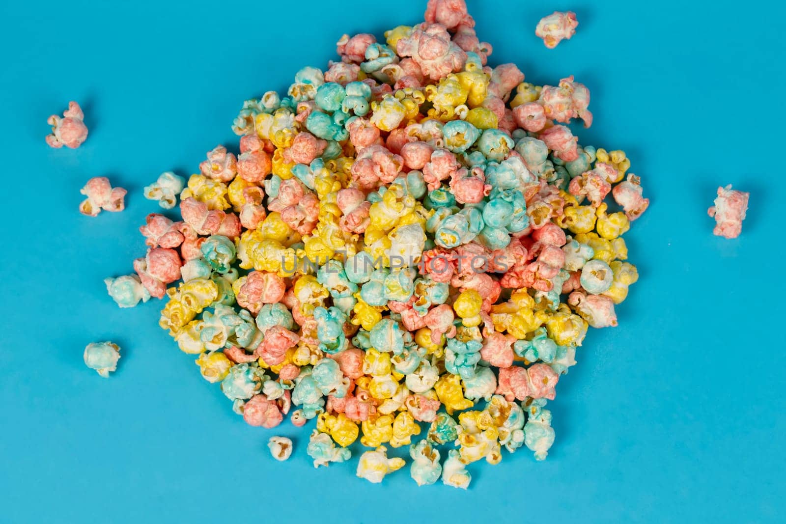Multi-colored popcorn is scattered on a blue background. Colorful beautiful sweet dessert.
