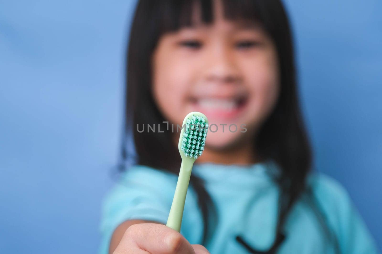 Smiling cute little girl holding toothbrush isolated on blue background. Cute little child brushing teeth. Kid training oral hygiene, Tooth decay prevention or dental care concept.