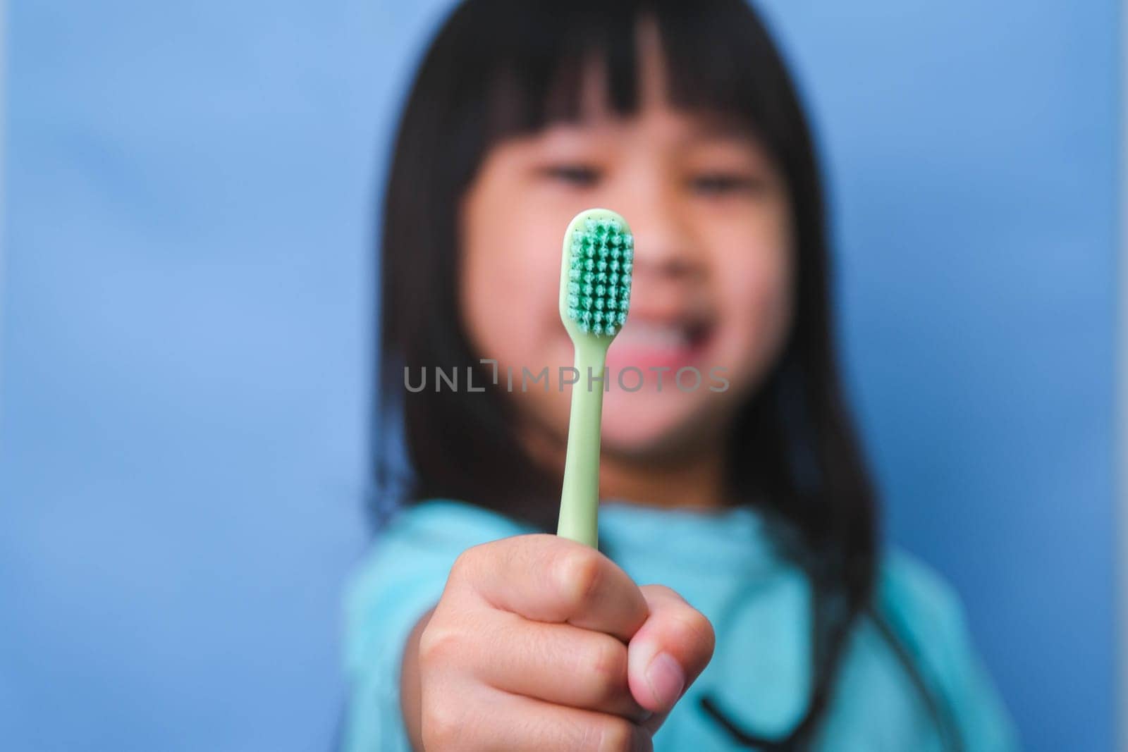 Smiling cute little girl holding toothbrush isolated on blue background. Cute little child brushing teeth. Kid training oral hygiene, Tooth decay prevention or dental care concept. by TEERASAK