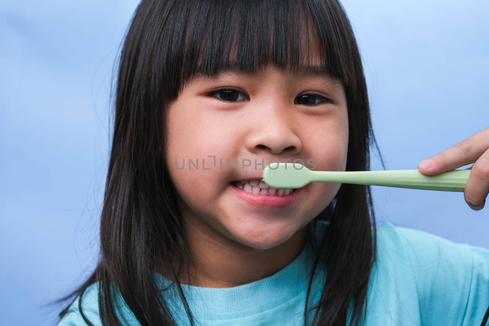 Smiling cute little girl holding toothbrush isolated on blue background. Cute little child brushing teeth. Kid training oral hygiene, Tooth decay prevention or dental care concept. by TEERASAK